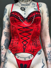 Front view of the red bustier and matching briefs, showing the long black ribbon lacing and broken-heart detail on the briefs.