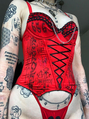 Angled view of the matching red bustier and briefs with black trim and chains, worn beneath layered styling necklaces.