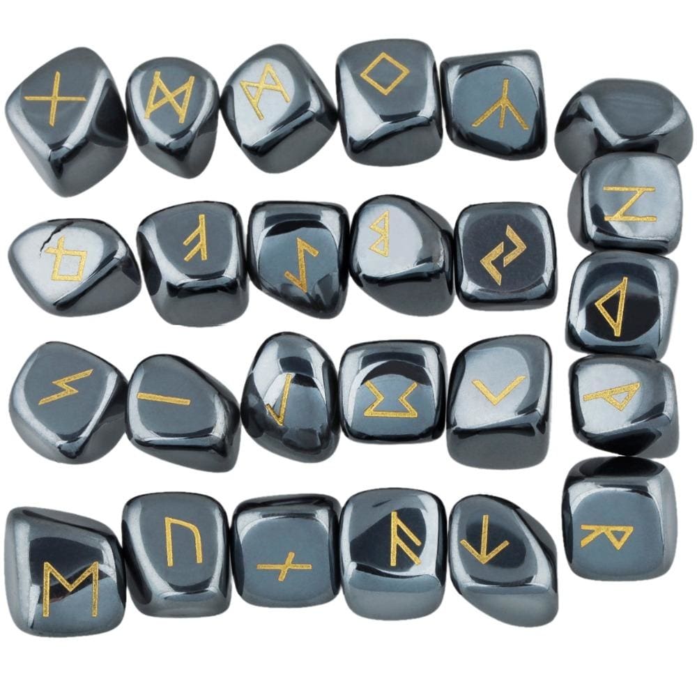 Hematite rune stone set laid out in rows, showing individual gold-coloured characters and one unmarked stone against dark metallic grey surfaces.