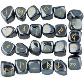 Hematite rune stone set laid out in rows, showing individual gold-coloured characters and one unmarked stone against dark metallic grey surfaces.