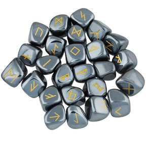 A loose pile of hematite rune stones with dark metallic grey surfaces, rounded edges and gold-coloured rune marks visible across the top.