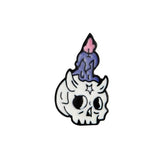 White horned skull enamel pin with a small star on its forehead and a dripping purple candle topped by a pink flame.
