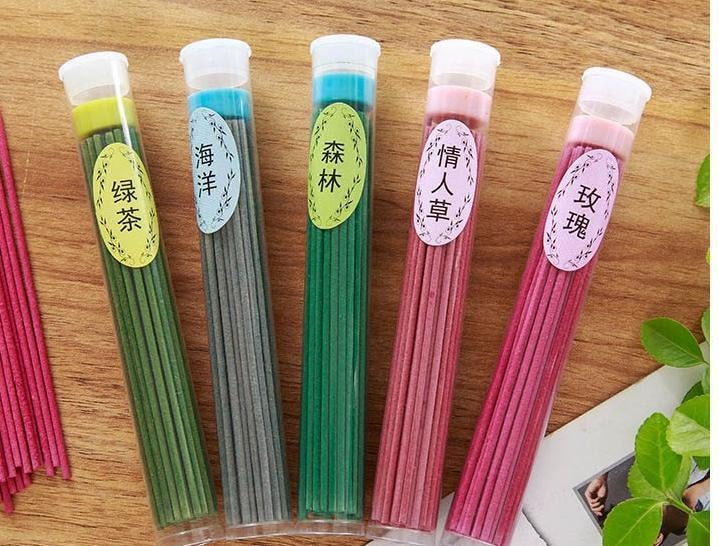 Five labelled tubes of incense sticks laid on a wooden surface, displaying green tea, ocean, forest, Desmodium gyrans and rose fragrances.