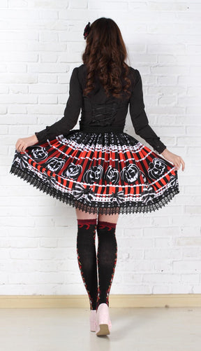 Rear outfit view of the red and black jack-o-lantern skirt held out at both sides, showing the continuing pumpkin print, bow illustrations and black lace edging.