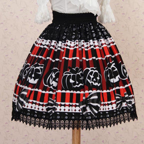 Jack-o-lantern skirt displayed with a separate white top against a pale patterned wall, showing the black waistband, red stripes and scalloped black lace edging.
