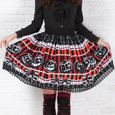 Red and black striped jack-o-lantern skirt held out to show its full shape, white pumpkin outlines and black lace hem. It is styled with a separate black blouse and patterned knee socks against a white brick wall.