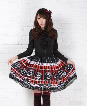 Front outfit view of the pumpkin print skirt spread gently at both sides, showing the wide black waistband and lace border beneath the jack-o-lantern faces.