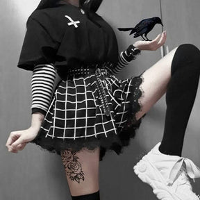 Raised-leg view of the short grid-print culotte skort, showing the divided flared shape and lace hem above a black thigh-high sock.
