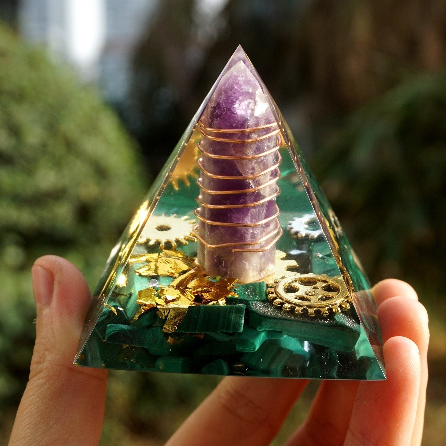 Malachite and amethyst orgone pyramid held in a hand, showing the complete clear outline around the wrapped purple point.