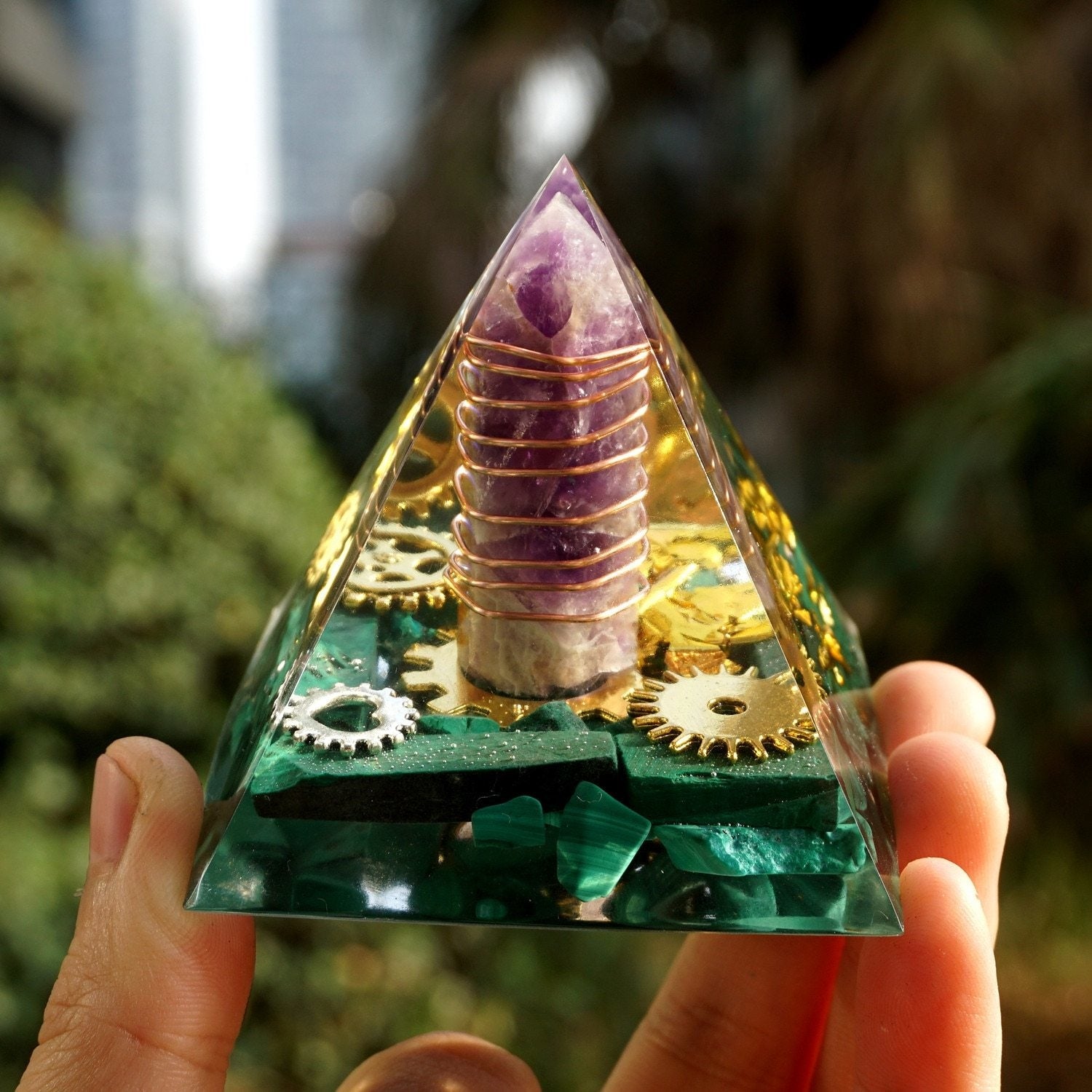 Angled front view of the amethyst point inside the malachite pyramid, with its warm spiral wrapping and small gear shapes visible.