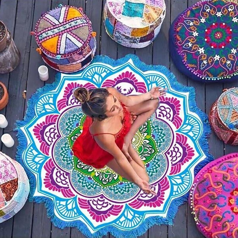 Blue and pink mandala flower throw seen from above beneath a woman in a red swimsuit, with patterned cushions beside the circular floral design.