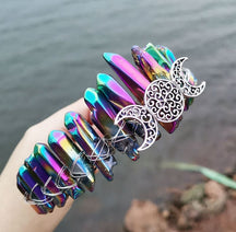 Angled view of a metallic rainbow crystal point crown with a silver-tone triple moon emblem and wire-wrapped band.