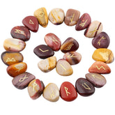 Mookaite rune stones arranged in a circle, with mustard, red and beige polished surfaces and gold-coloured characters. The set includes a blank stone.