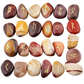 Mookaite rune stone set laid out in rows, showing individual gold-coloured characters and one unmarked stone against mustard, red and beige surfaces.