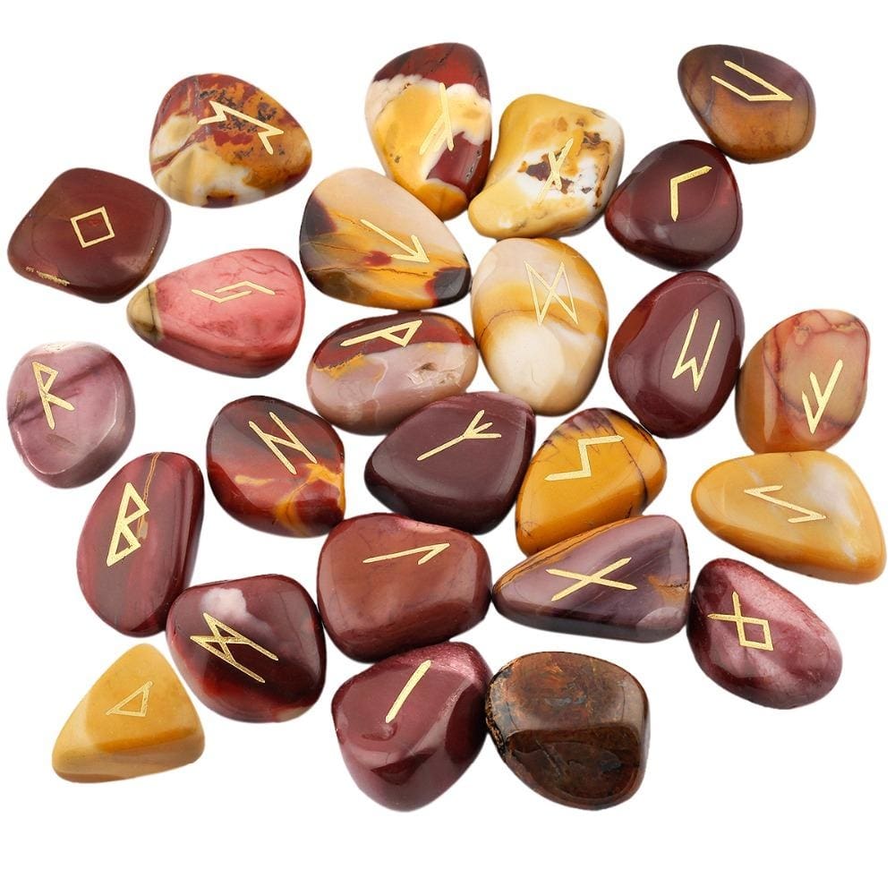 A loose pile of mookaite rune stones with mustard, red and beige surfaces, rounded edges and gold-coloured rune marks visible across the top.