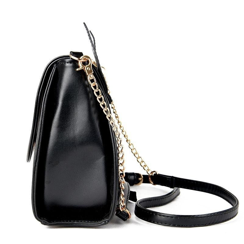 Side profile of the black cat-ear shoulder bag, with a curved flap edge, gold-tone chain and long black strap.