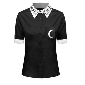 Front view of the black Moon Child short-sleeve blouse on a white torso form, with black buttons, a white lettered collar and a crescent moon chest pocket.