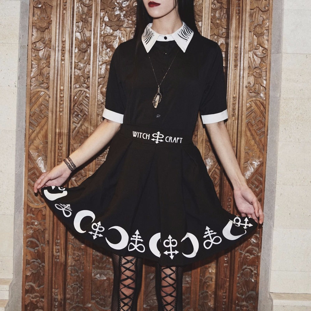 Moon Child blouse styled with a separate black printed skirt, pendant and lace-up legwear in front of a carved wooden screen. Its white collar and cuffs repeat the pale details in the outfit.