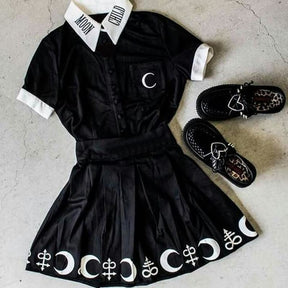 Flat outfit arrangement of the black Moon Child blouse with a separate symbol-print skirt and shoes on a gray surface, showing the white collar, cuffs and crescent pocket.
