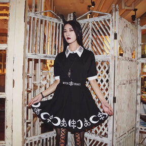 Black Moon Child blouse and separate symbol-print skirt worn in front of a pale wooden screen, with the white collar visible above a long pendant.