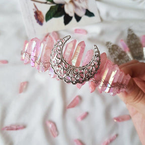 Pink rose quartz crown with a silver-tone filigree moon, shown beside pink flowers.