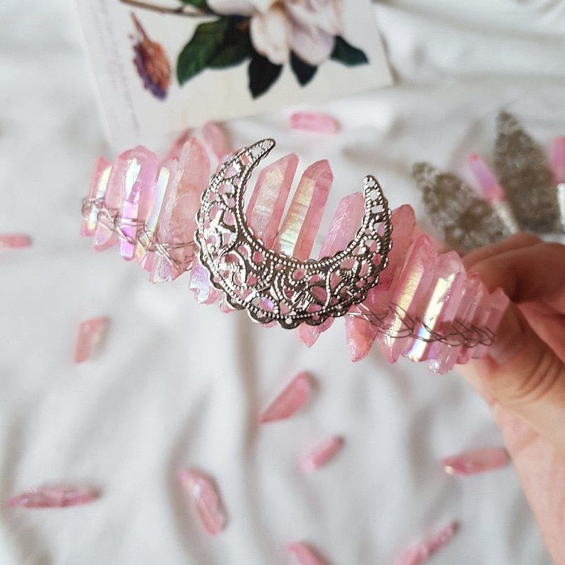 Pink rose quartz crown with a silver-tone filigree moon, shown beside pink flowers.