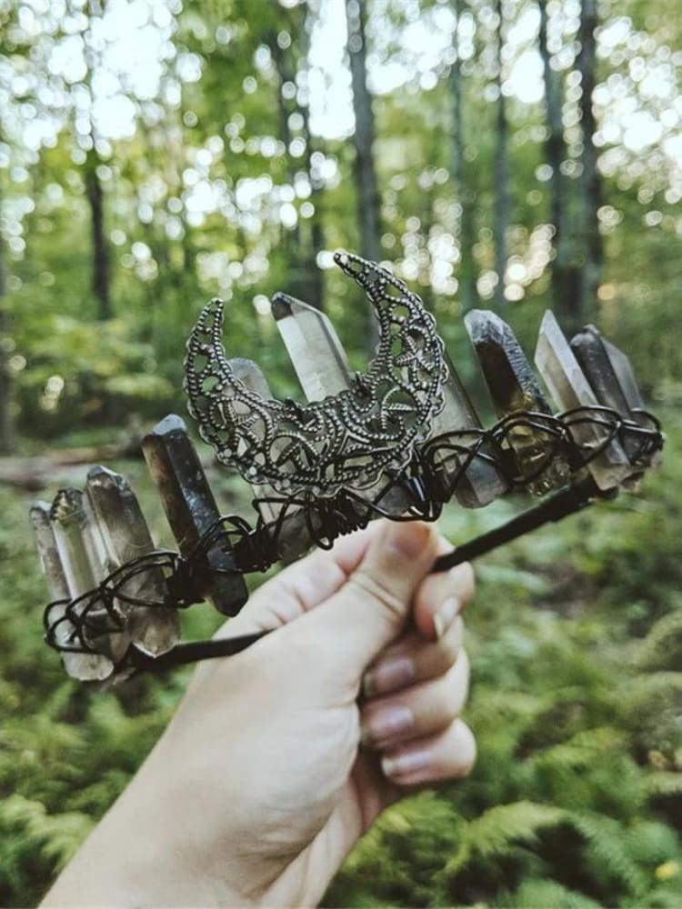 Smoky quartz point crown with an antique-tone filigree crescent held against a woodland background.