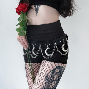 Black Mooncraft belt worn low over a black mini skirt and fishnet tights. Silver-tone crescent moons and draped chains hang below the strap as the model holds a red rose.