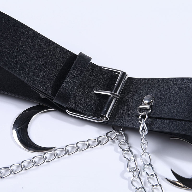 Detail of the black strap, rectangular pin buckle and belt keeper, with a silver-tone crescent and chain links arranged on the white surface below.