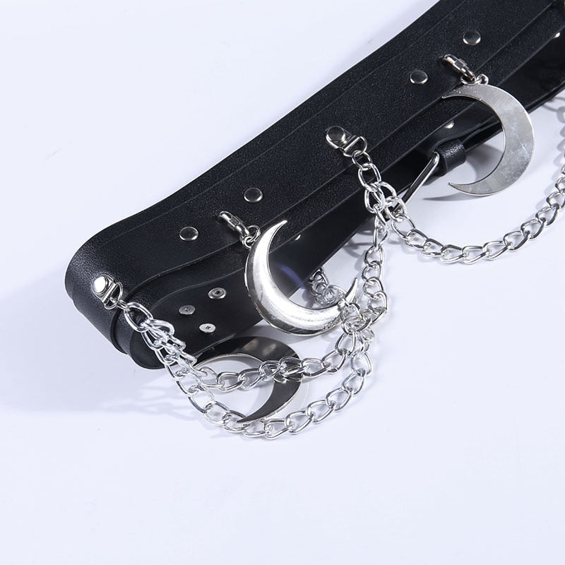Close-up of the black belt folded diagonally on white, showing the metal crescents, chain links, riveted attachments and adjustment holes.