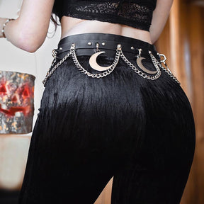 Mooncraft belt styled at the waist of black trousers beneath a lace crop top. The silver-tone crescent moons and draped chains contrast with the dark outfit.