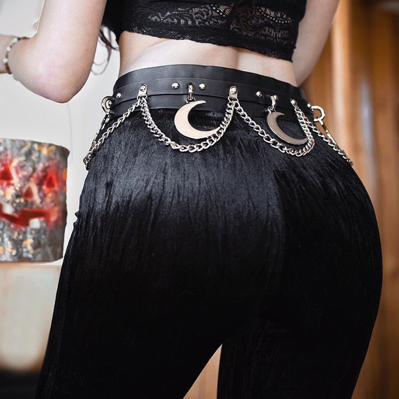 Mooncraft belt styled at the waist of black trousers beneath a lace crop top. The silver-tone crescent moons and draped chains contrast with the dark outfit.