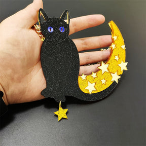 Large black cat and gold crescent pendant resting across an open hand, showing blue eyes, fine glitter, raised star details and the dangling gold star.