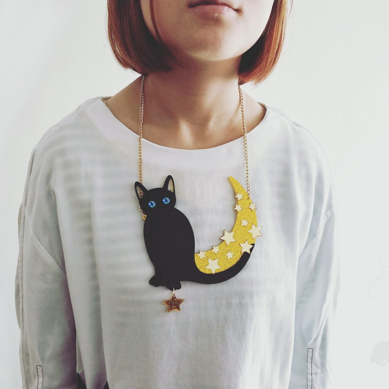 Black cat and glitter crescent statement necklace worn over a plain white top, showing its broad pendant shape and dangling star below the gold-tone chain.