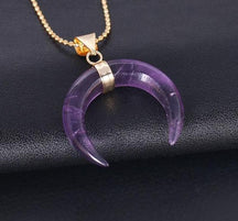 Purple amethyst crescent pendant on a dark background, with a gold-tone band at its centre and a fine ball chain.