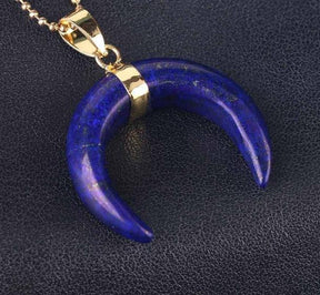 Deep blue lapis lazuli crescent pendant with scattered stone markings and a gold-tone ball chain.