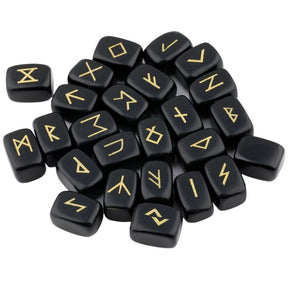 A loose pile of obsidian rune stones with glossy black surfaces, rounded edges and gold-coloured rune marks visible across the top.
