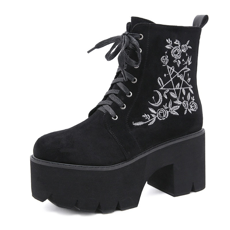 Black platform ankle boots with white pentagram, moon and rose embroidery shown from an angled front view.
