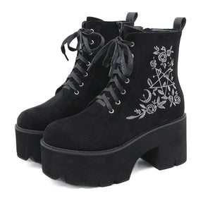 Black platform ankle boots with white pentagram, moon and rose embroidery shown as a pair at a three-quarter angle.