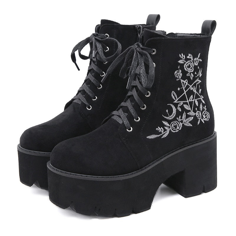 Black platform ankle boots with white pentagram, moon and rose embroidery shown as a pair at a three-quarter angle.