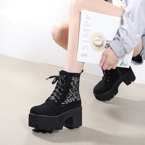 Black platform ankle boots with white pentagram, moon and rose embroidery shown in a wider crouching outfit view.