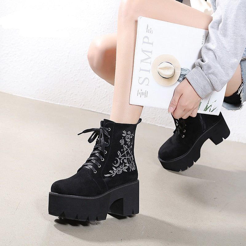 Black platform ankle boots with white pentagram, moon and rose embroidery shown in a wider crouching outfit view.