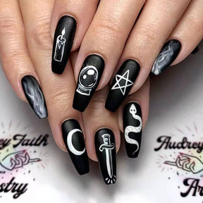 Alternate framing of the black occult coffin nails worn on a hand, with white mystical artwork including a candle, crystal ball, pentagram and snake.