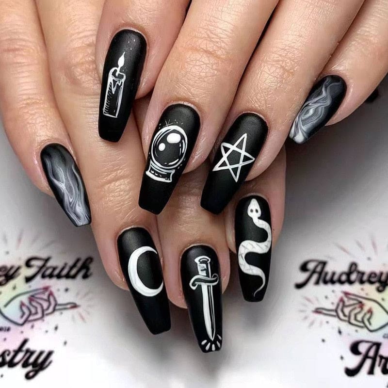 Black occult press-on nails worn on a hand, showing squared coffin tips with white mystical symbols and wisps of pale smoke. A candle, crystal ball, snake and pentagram appear across the set.
