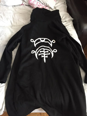Black hooded cardigan laid face down on bedding, showing the large white occult-style graphic centered on the back and the long plain sleeves.