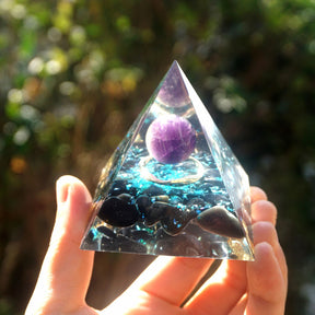 Additional view of Ocean amethyst orgone pyramid with a purple sphere, blue flakes and dark obsidian stones. A repeated sunlit view shows the circular metal detail beneath the sphere.