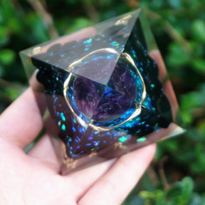 Ocean amethyst orgone pyramid with a purple sphere, blue flakes and dark obsidian stones. Viewed from above to show the purple sphere and circular metal detail.