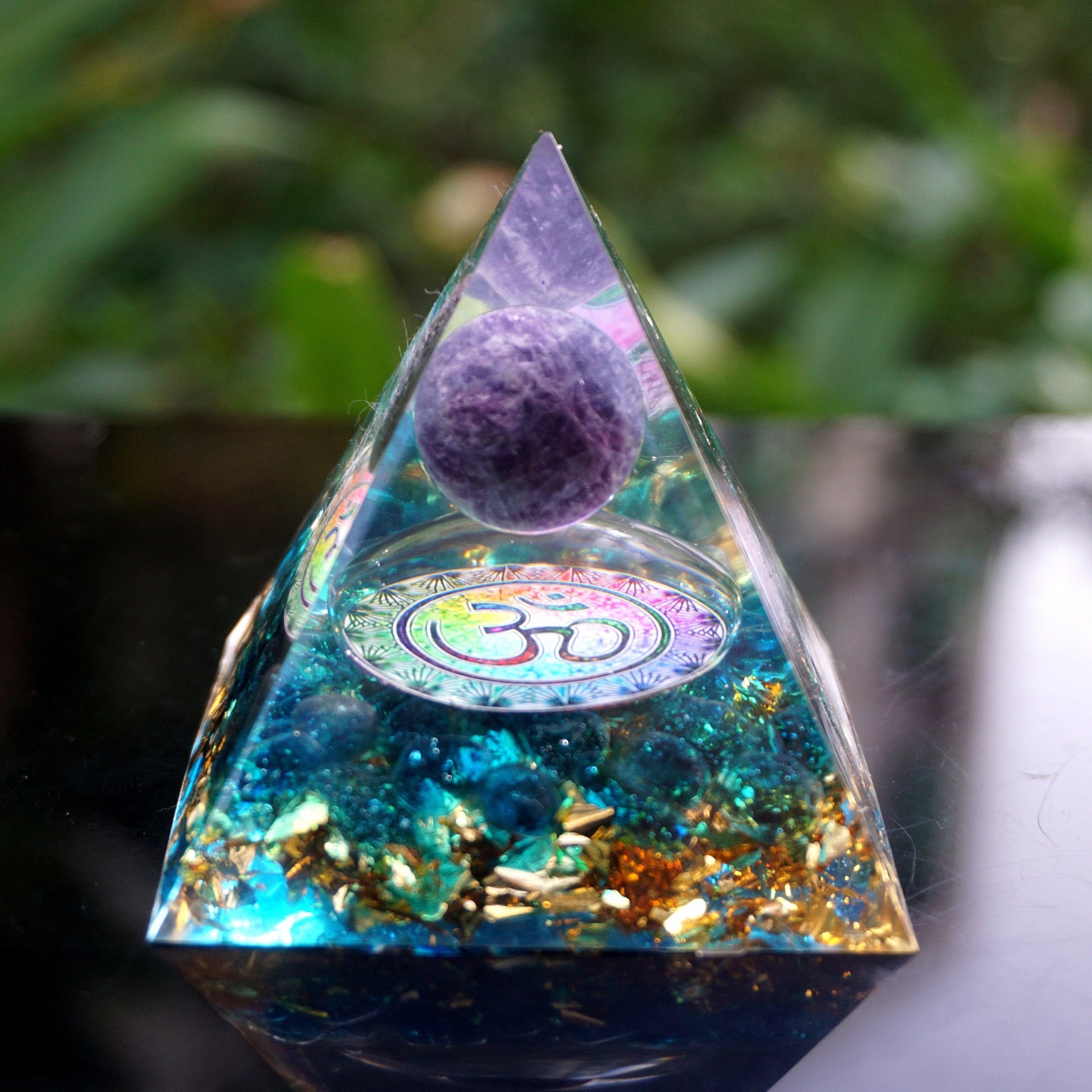 Full view of a clear Om pyramid with amethyst and blue quartz, displayed upright on a wooden surface.
