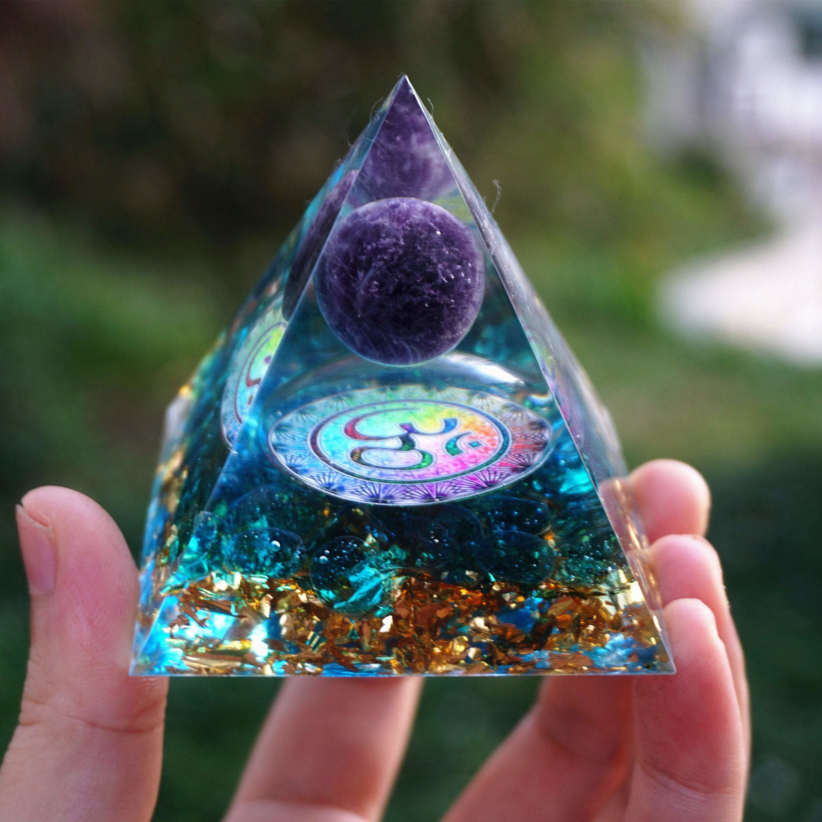 Om amethyst pyramid held on an open hand, showing the clear pointed outline, purple sphere and blue stone-filled base.