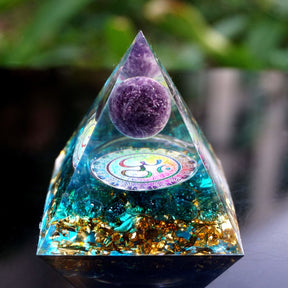 Front detail of the Om pyramid on wood, showing the purple sphere above the metallic symbol and blue crystal pieces.